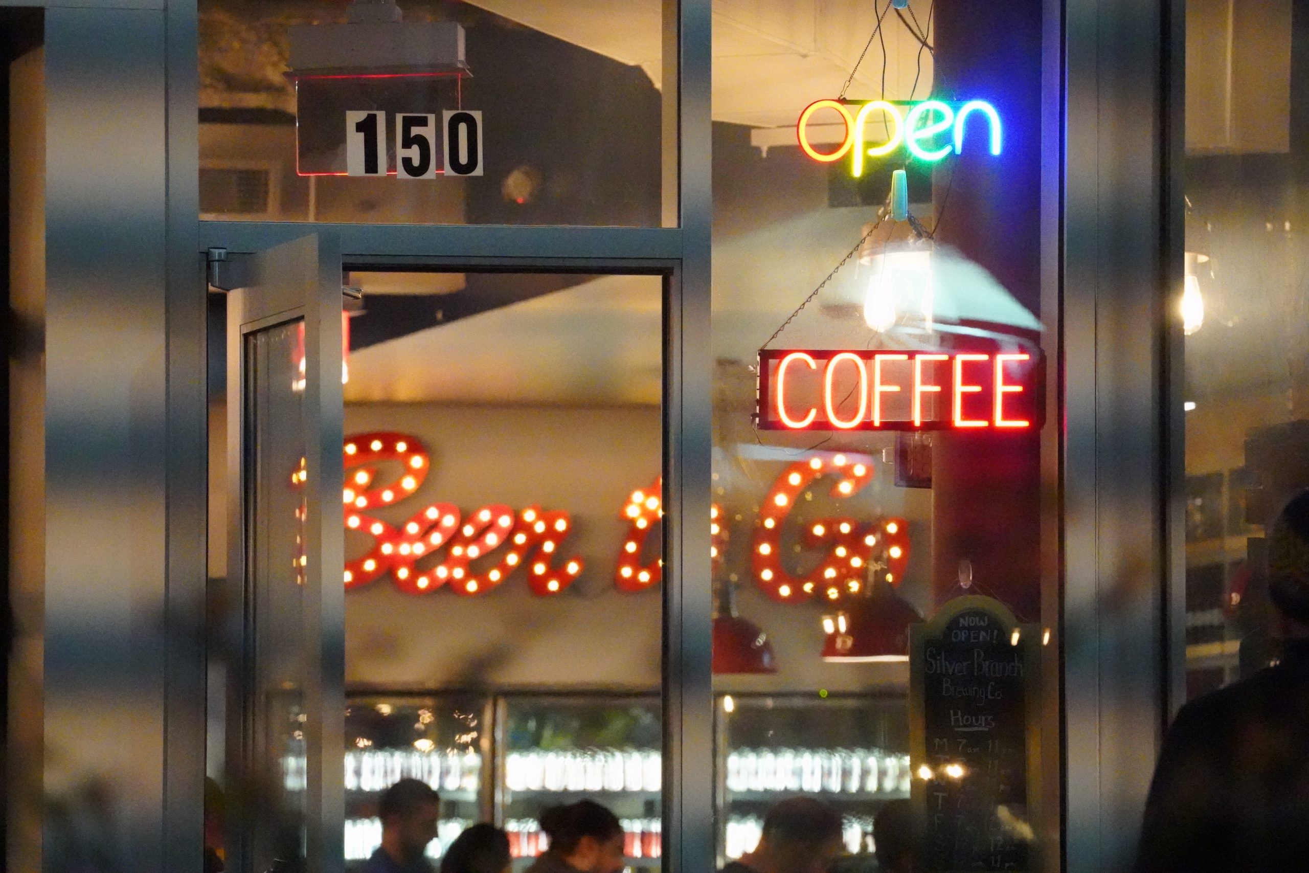 Open doorway to the Silver Branch brewery with a light bulb sign displaying Beer to Go in large letters in the background.