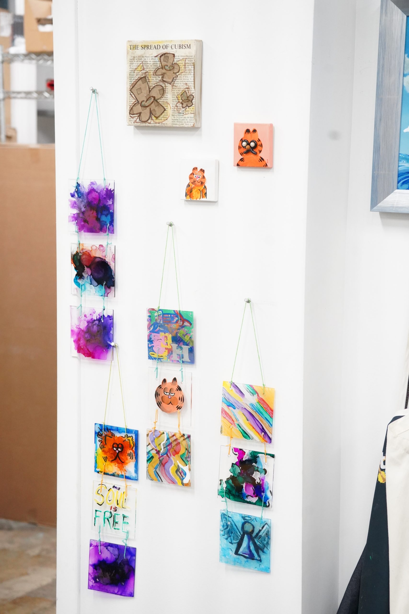 Various small Garfield from memory miniature portraits hanging from string on a wall.